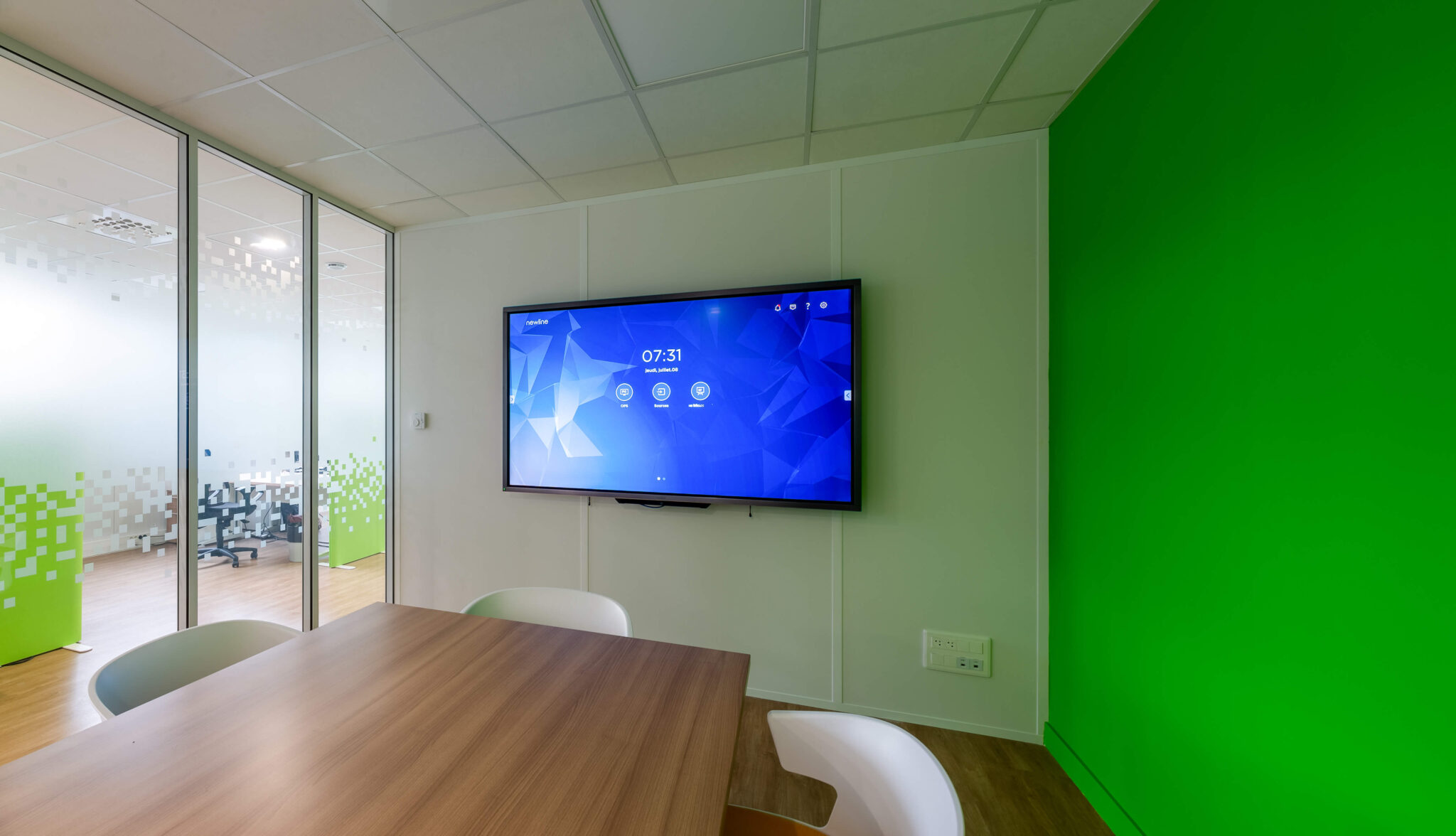 Salle de réunion avec pan de mur vert et vue sur les bureaux via une cloison vitrée